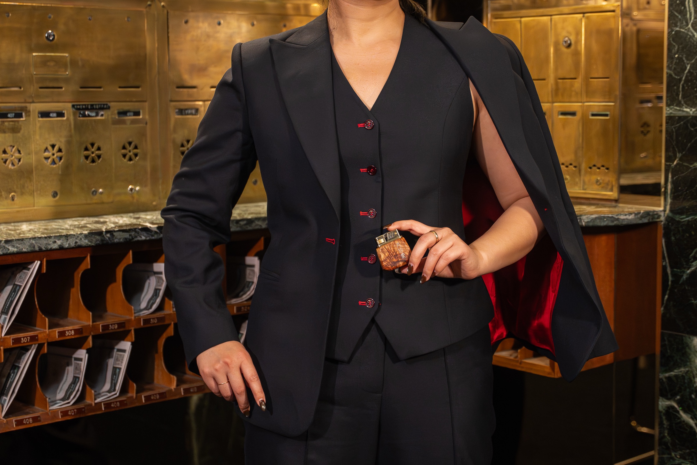 A tailored navy three-piece suit with oxblood buttons and red silk lining, in a vintage brass-and-marble lobby.